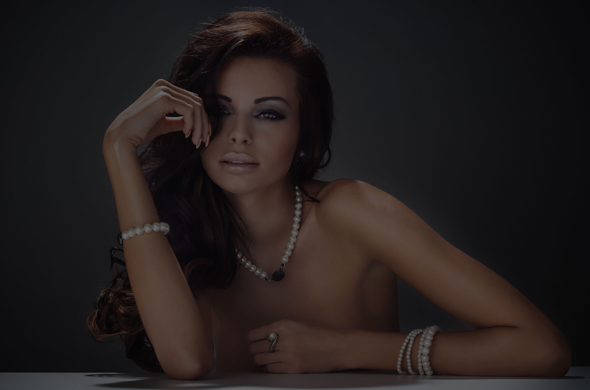 Beautiful woman wearing pearl jewelry resting arms on table showing beautiful arms.